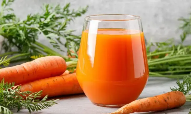 Un vaso de jugo de zanahoria fresco junto a zanahorias enteras. Descubre para qué es buena la zanahoria: ¡salud y vitalidad!