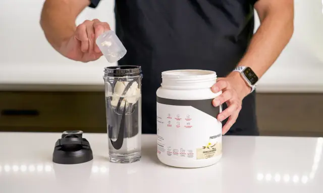 Hombre prepara batido con proteína en polvo para ganar músculo. El envase indica para qué sirve la proteína en polvo: energizar y recuperación post-entreno.