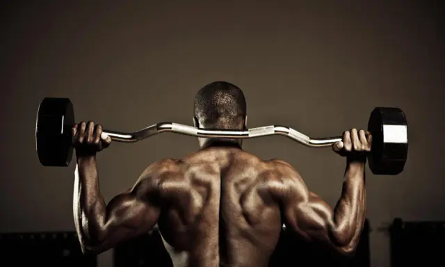 Hombre musculoso con barra detrás del cuello, trabajando para fortalecer lumbares.