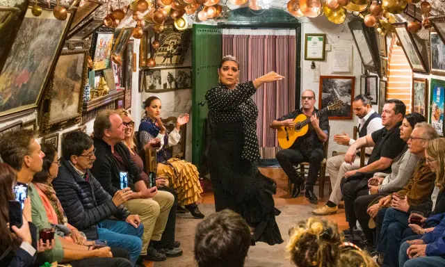 Una bailaora de flamenco, con un vestido negro de lunares, actúa en un local íntimo donde se baila flamenco. Un guitarrista la acompaña.