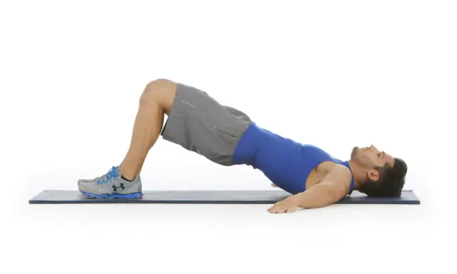 Hombre realizando puente de glúteo, un ejercicio clave para fortalecer la zona lumbar en el gym.