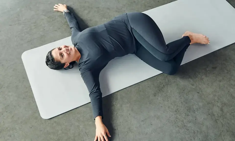 Mujer sonriente practicando ejercicios de yoga para relajarse, en posición de torsión acostada.