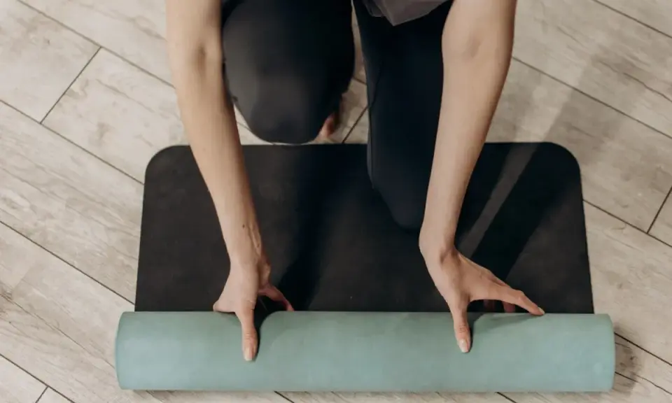 Manos enrollando una esterilla de yoga verde sobre una esterilla negra. Un paso esencial para saber como limpiar esterilla yoga y mantenerla en buen estado.