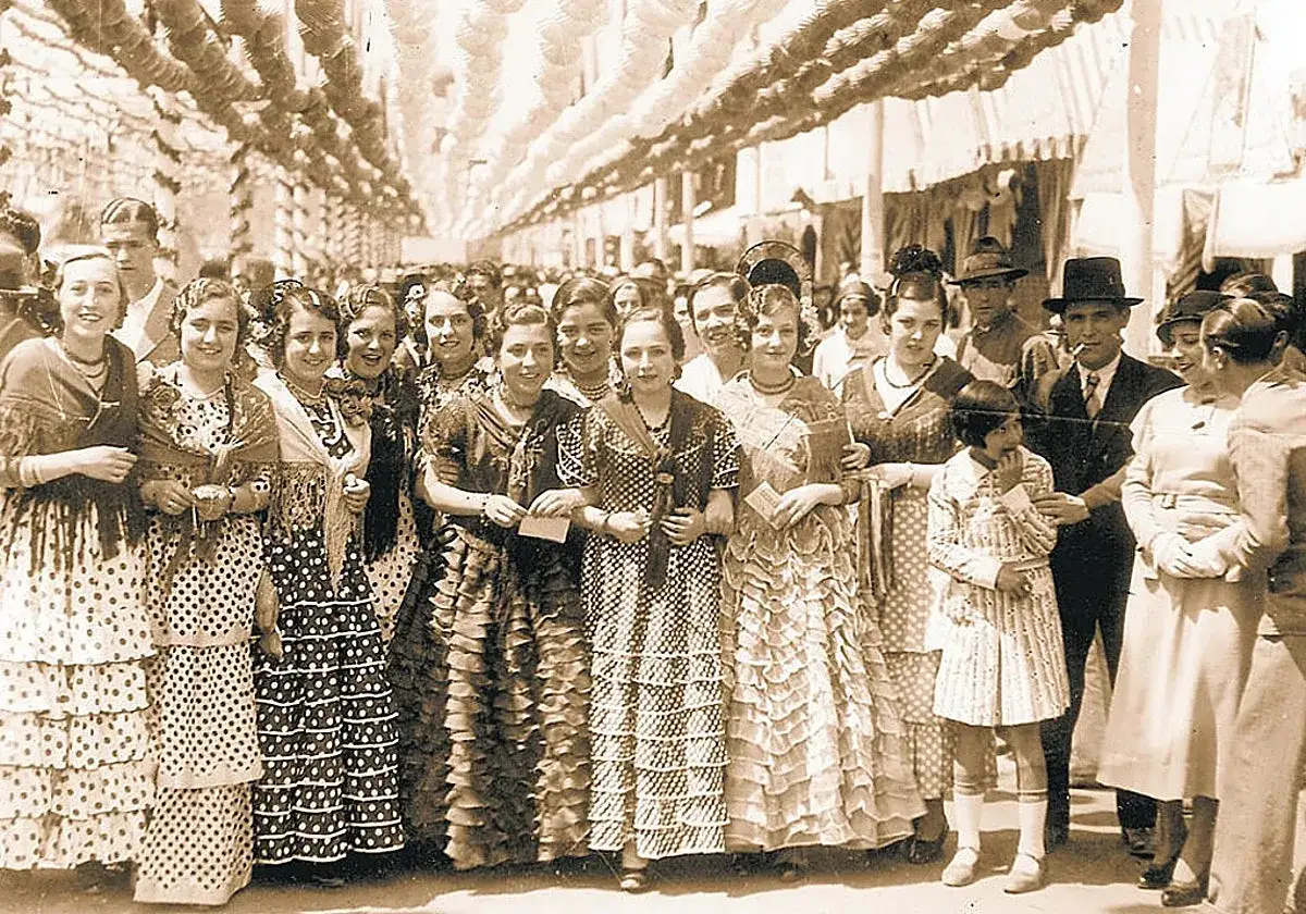 Un grupo de mujeres y ni&ntilde;as, algunas con trajes de flamenca, celebran en una feria. Un vistazo a la historia del traje de flamenca.