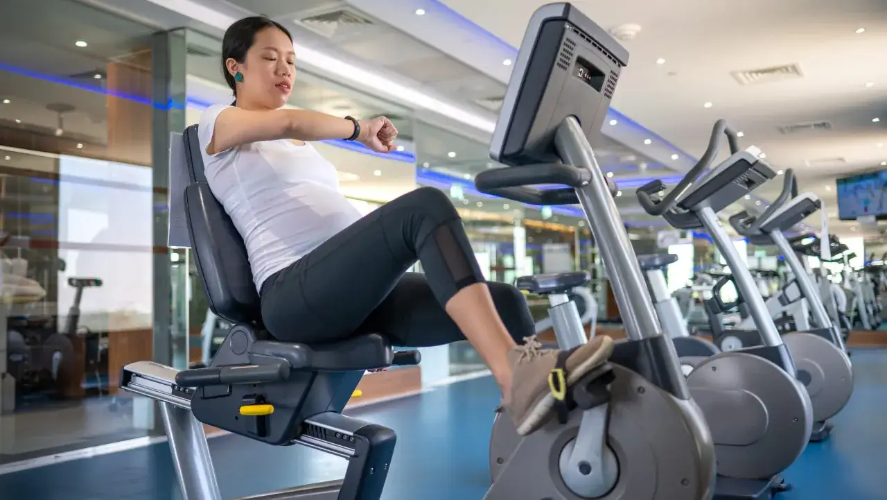 Embarazada en el gym, pedaleando en bicicleta est&aacute;tica. Ejercicios seguros para embarazadas en el gym.