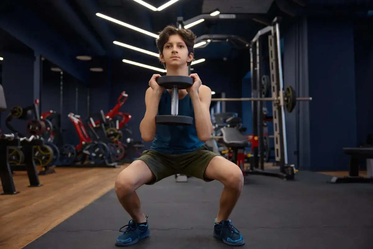 Adolescente de 15 a&ntilde;os haciendo sentadillas con mancuerna, parte de sus rutinas de gimnasio para adolescentes de 15 a&ntilde;os.