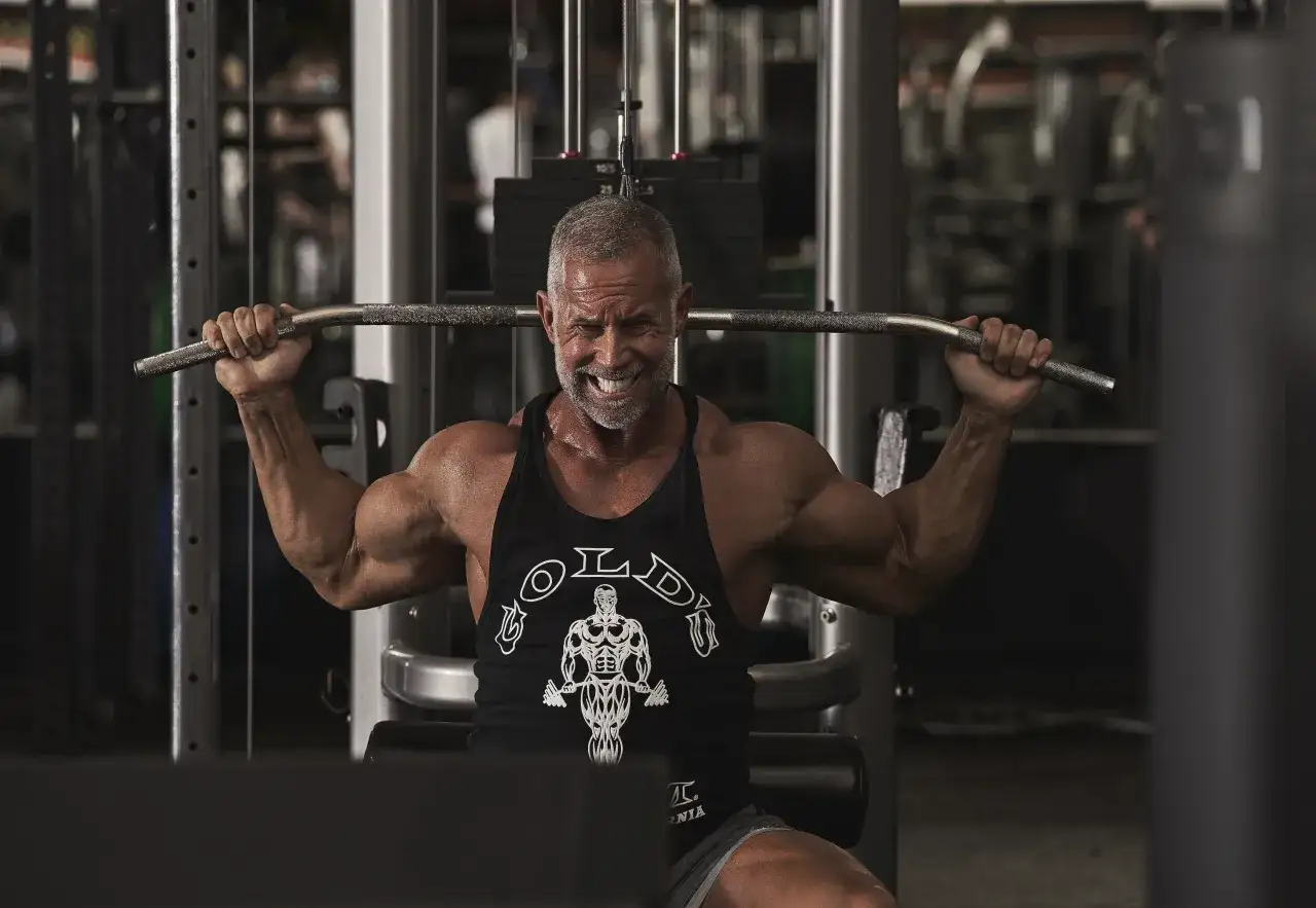 Hombre musculoso sonriendo mientras realiza ejercicios de espalda en el gym, concentrado en su entrenamiento.