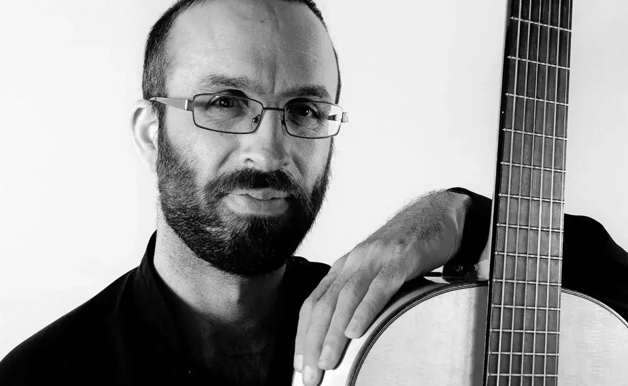 Guitarrista flamenco andaluz con barba y gafas, apoyado en su guitarra.