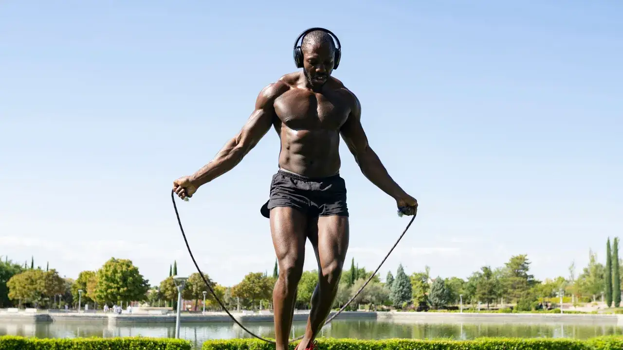 Hombre musculoso salta a la comba con auriculares, disfrutando de los beneficios de saltar a la comba al aire libre.