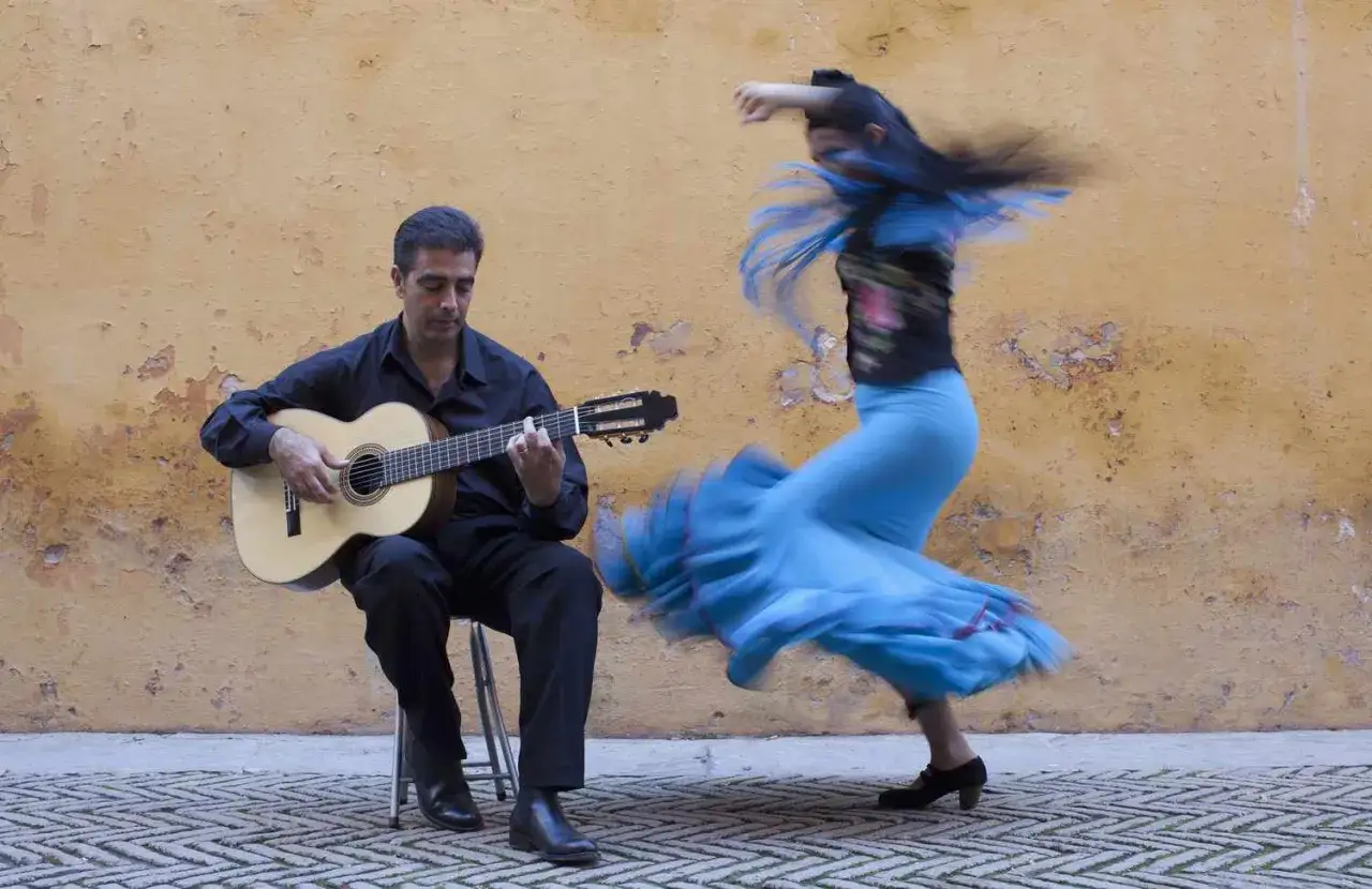 Hombre toca guitarra mientras mujer realiza vibrantes bailes flamencos con su falda azul ondeando.