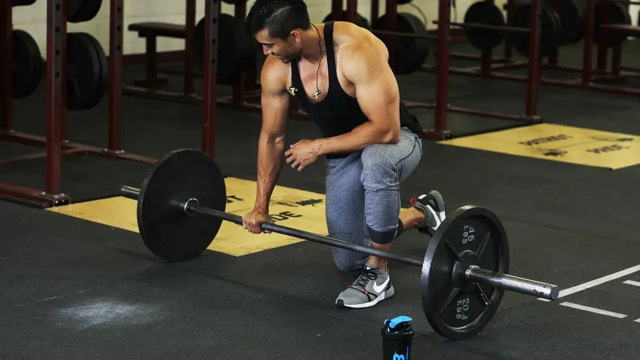 Hombre en el gimnasio, arrodillado, listo para levantar una barra. Un paso clave para saber como ganar masa muscular.