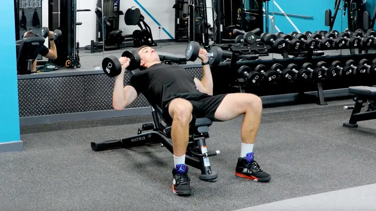 Hombre haciendo press inclinado que trabaja con mancuernas en un gimnasio.