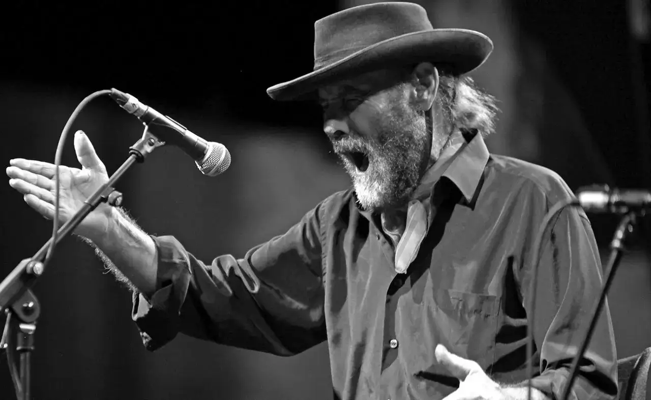 Hombre con sombrero y barba canta apasionadamente al micr&oacute;fono, transmitiendo las mejores letras flamenco.