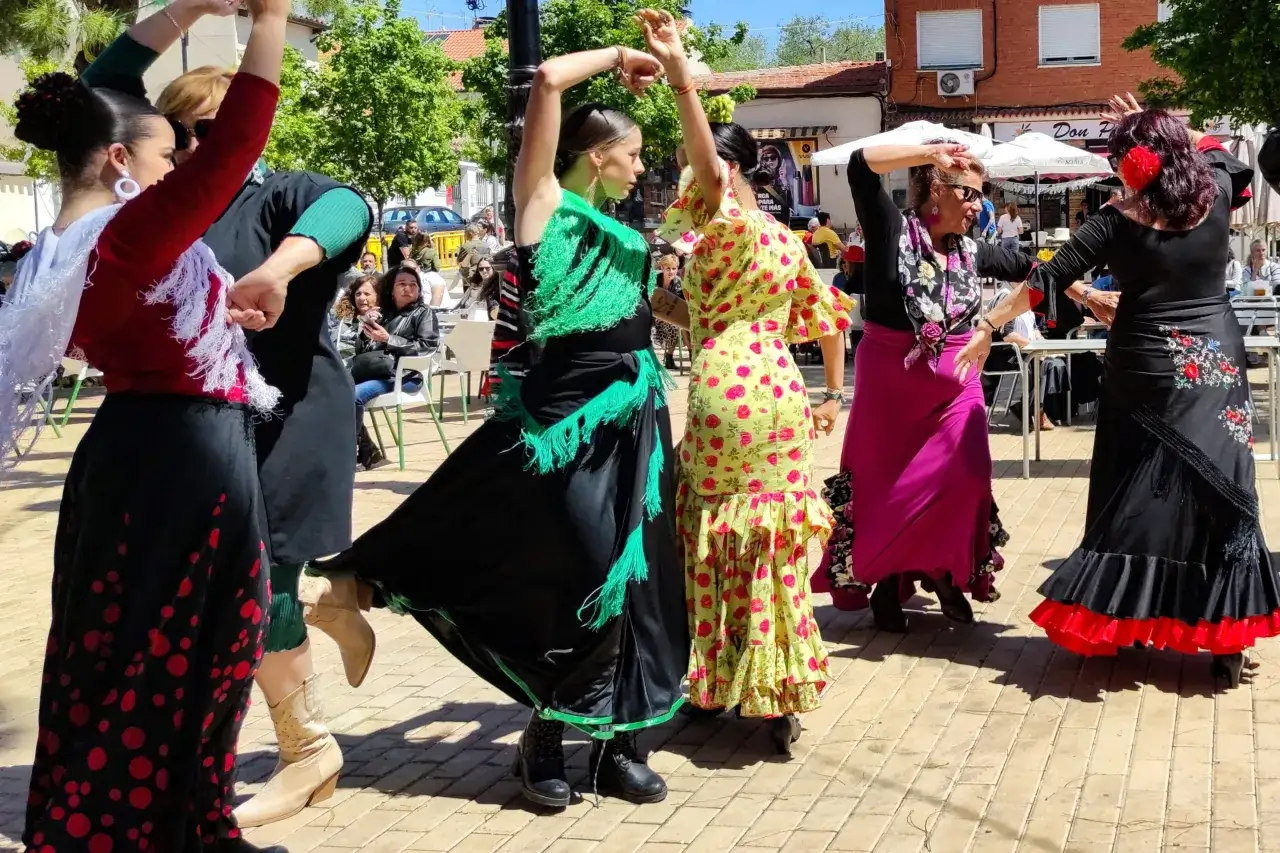 Grupo de sevillanas hombre y mujer bailando flamenco al aire libre. Vestidos coloridos y movimiento de faldas.