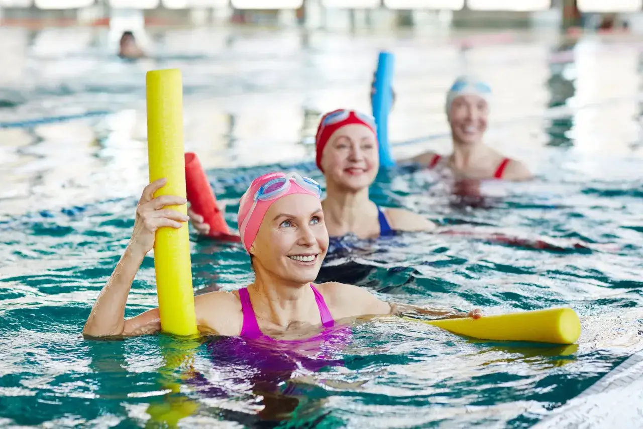 Mujeres sonriendo en una piscina, usando flotadores. Nadar es cardio o fuerza, y ellas disfrutan del ejercicio acu&aacute;tico.