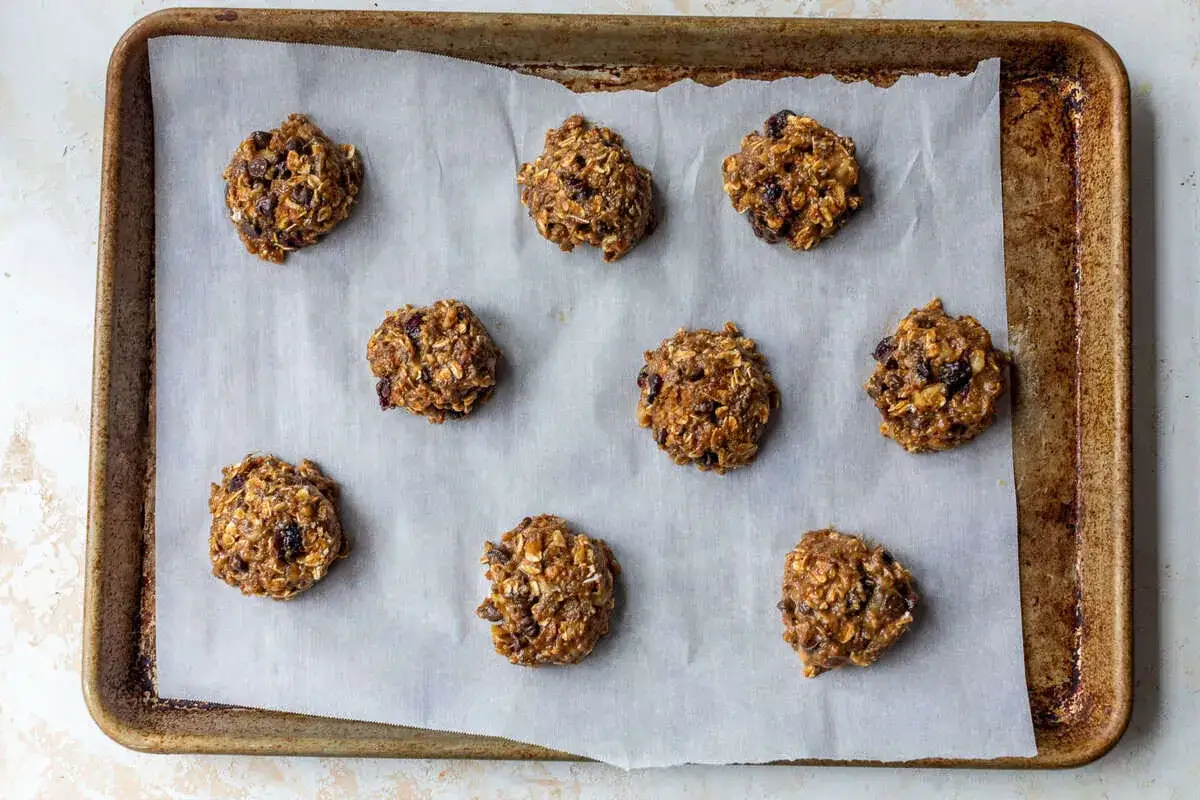 Nueve galletas proteicas receta, con avena y pasas, listas para hornear en una bandeja.