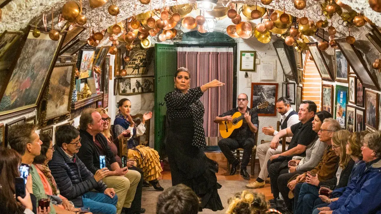 Una bailaora de flamenco, con un guitarrista y una cantaora, act&uacute;a en un local &iacute;ntimo donde se baila flamenco. El p&uacute;blico observa atentamente.