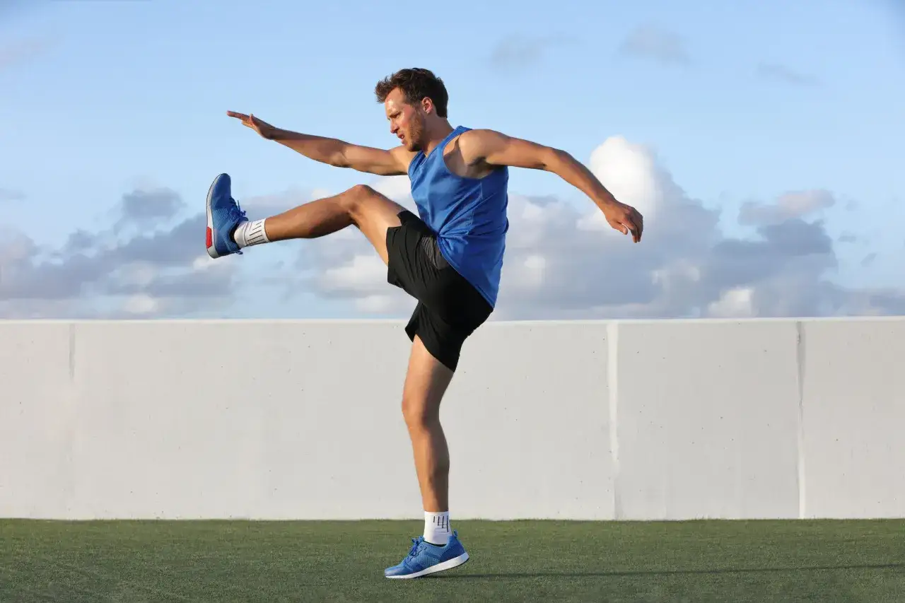 Hombre haciendo calentamiento de piernas con movimiento de patada frontal.