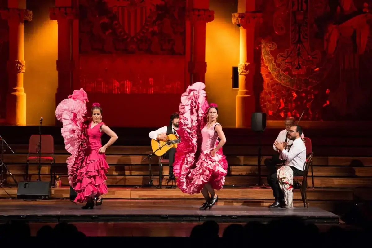 Bailaora flamenca famosa, con volantes rosas, danza al son de la guitarra y el cajón.