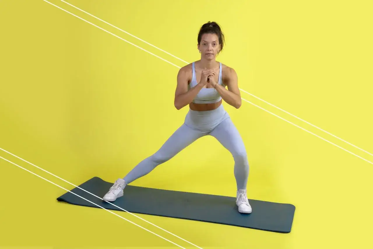 Mujer realizando zancada lateral en una esterilla, con las manos juntas frente al pecho.