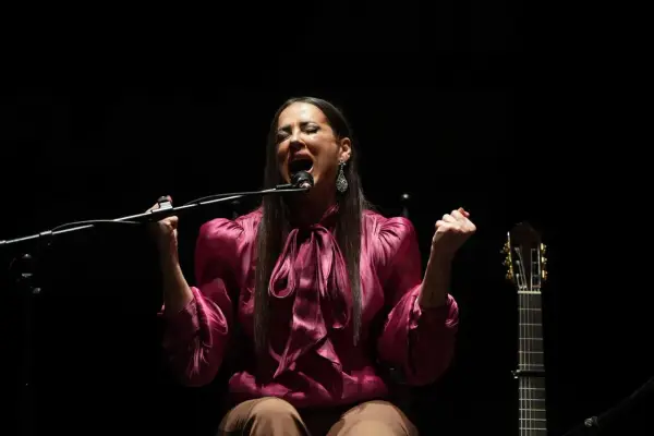 Cantante flamenco mujer, con el alma desbordada, canta apasionadamente frente al micrófono. A su lado, una guitarra espera.