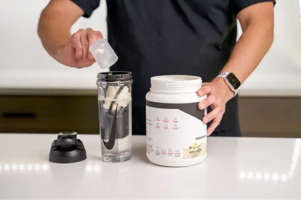 Hombre prepara batido con proteína en polvo para ganar músculo. El envase indica para qué sirve la proteína en polvo: energizar y recuperación post-entreno.
