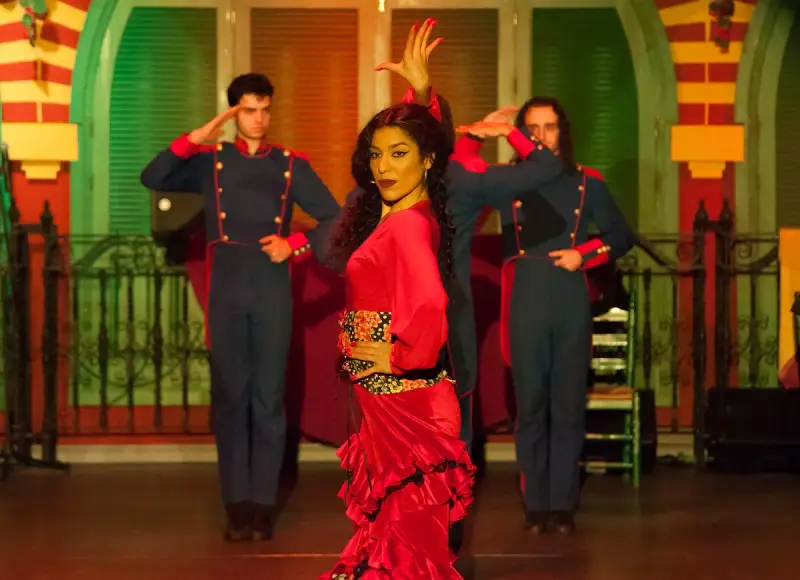 Una bailaora de flamenco con un vestido rojo vibrante, rodeada por dos hombres con uniformes militares, capturando la esencia de las alegrías flamenco.